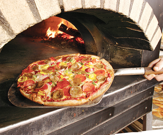supreme pizza pulled from a wood fire oven